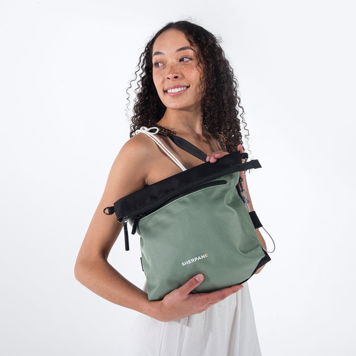 A woman holding Sherpani Vale Aloe Mist Green Anti-theft Reversible Crossbody around her shoulder with the front folded over. #color_aloe-mist-green