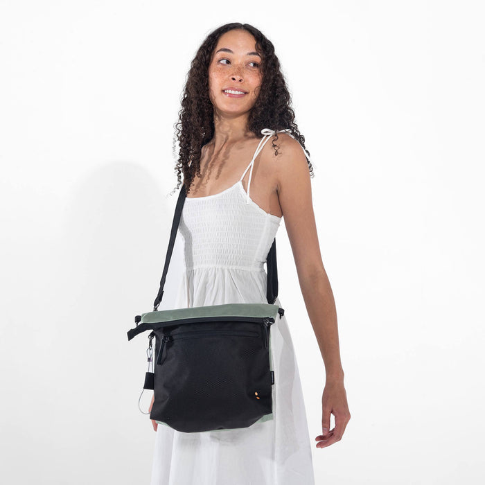 A woman holding Sherpani Vale Aloe Mist Green Anti-theft Reversible Crossbody around her shoulder with the front folded over. #color_aloe-mist-green