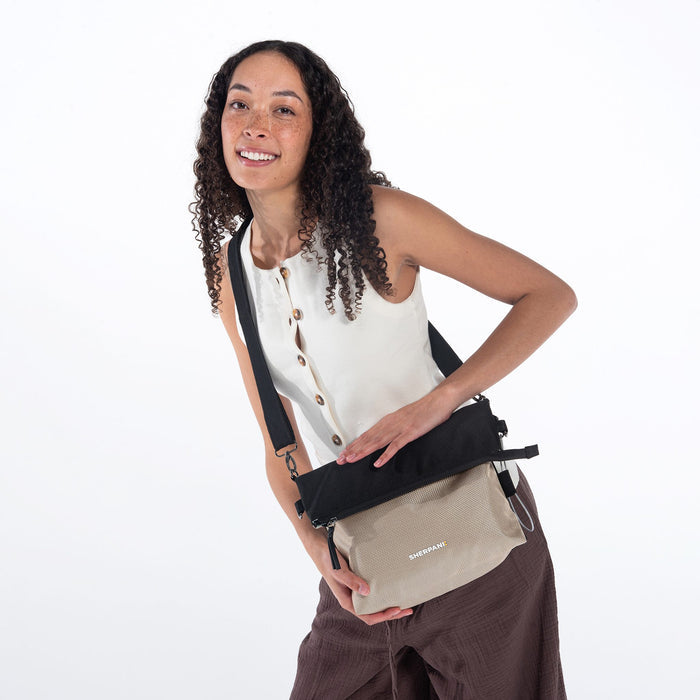 A woman holding Sherpani Vale Straw Beige Anti-theft Reversible Crossbody around her shoulder with the front folded over. #color_straw-beige