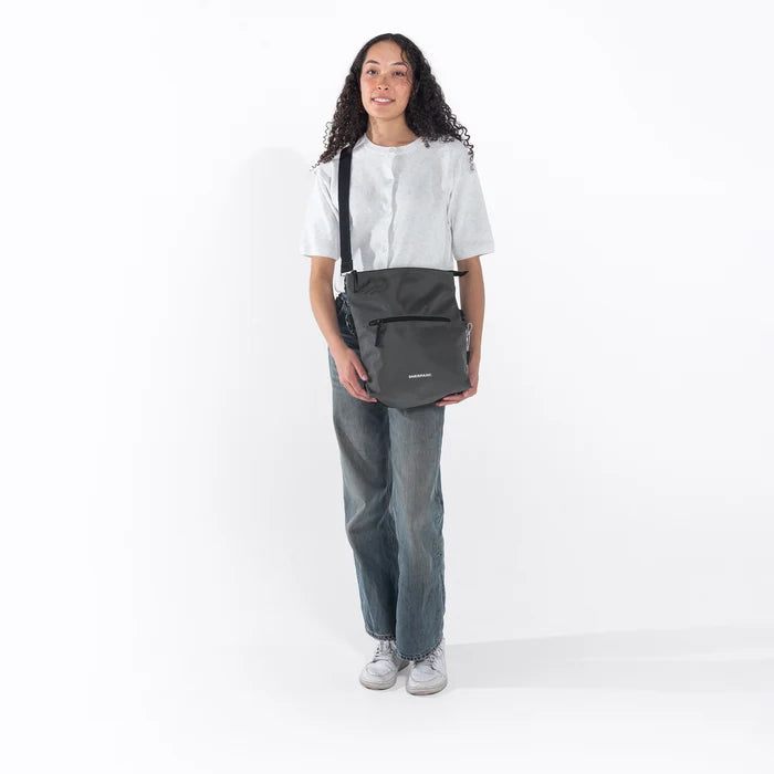 Woman wearing a Sherpani Vale Granite Anti-theft Reversible Crossbody against white background. #color_granite-grey