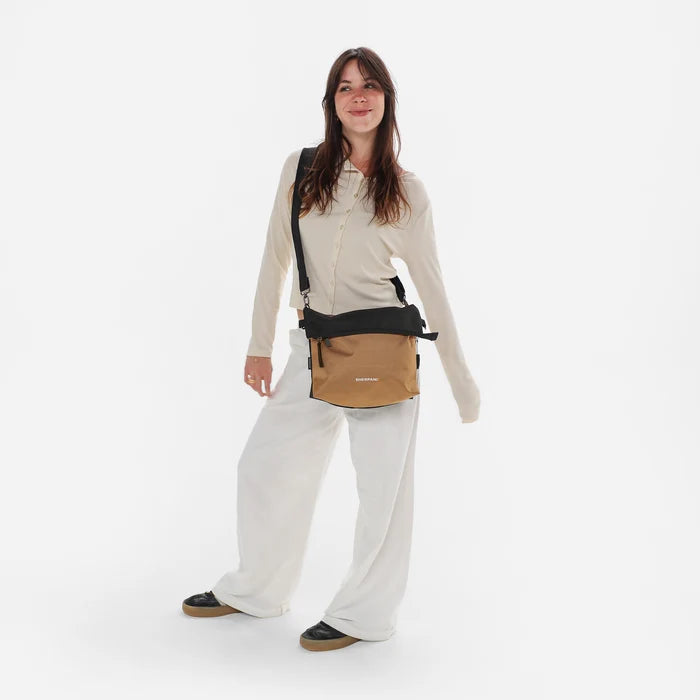 Woman wearing a Sherpani Vale Sand Anti-theft Reversible Crossbody against white background. #color_sand-tan