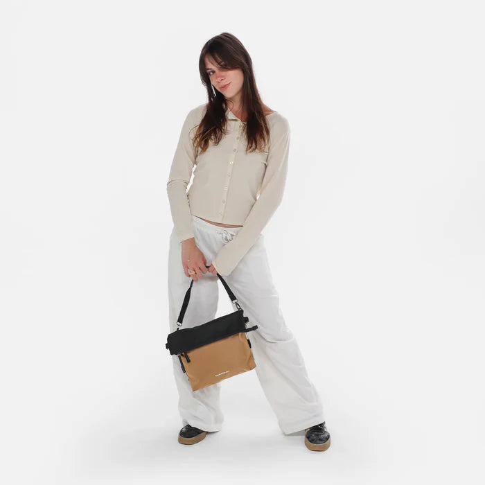Woman wearing a Sherpani Vale Sand Anti-theft Reversible Crossbody against white background. #color_sand-tan