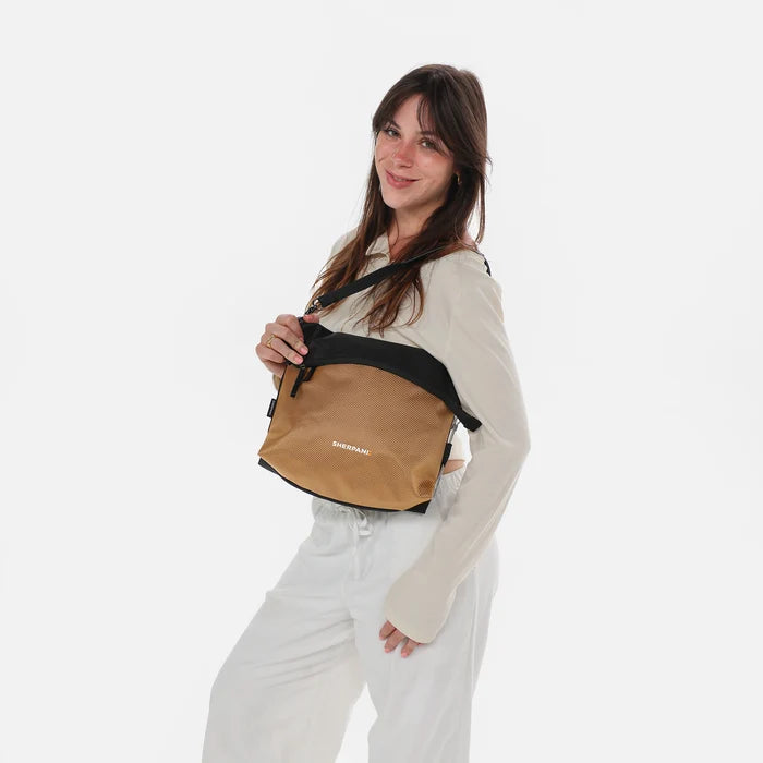 Woman wearing a Sherpani Vale Sand Anti-theft Reversible Crossbody against white background. #color_sand-tan