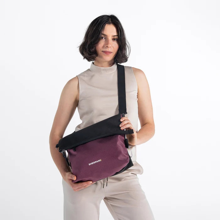 Woman wearing a Sherpani Vale Smoky Orchid Anti-theft Reversible Crossbody against white background. #color_smoky-orchid-pink