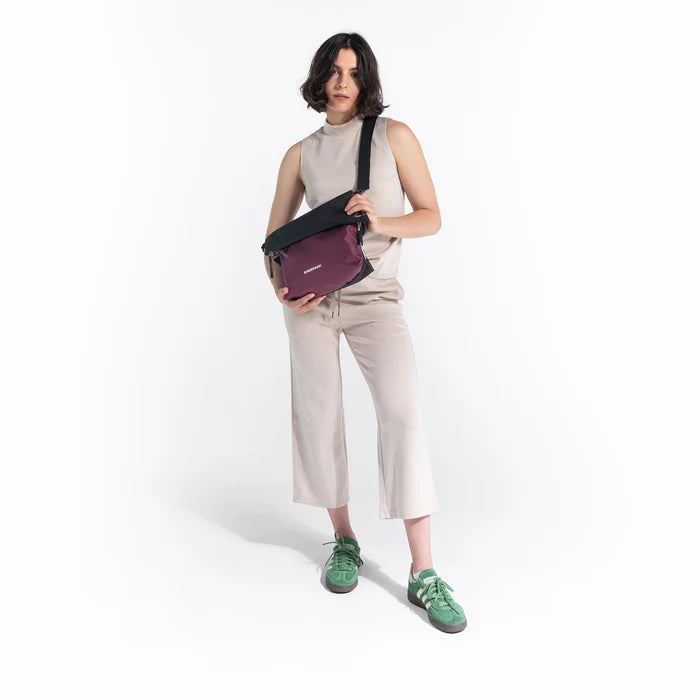 Woman wearing a Sherpani Vale Smoky Orchid Anti-theft Reversible Crossbody against white background. #color_smoky-orchid-pink