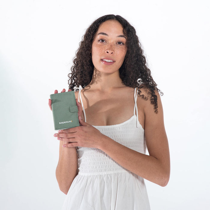 A woman holding a Sherpani Vienna Aloe Mist Green Anti-theft Passport Wallet against a white background.  #color_aloe-mist-green