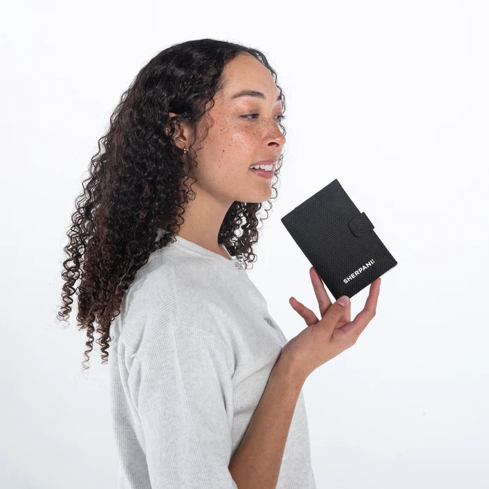 Woman holding a Sherpani Vienna Carbon Black Anti-theft Passport Wallet against white background. #color_carbon-black