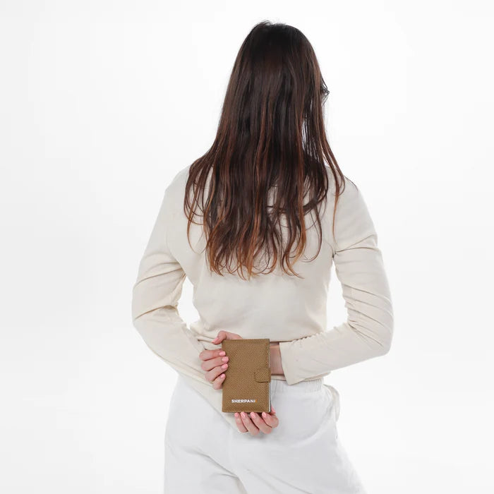 Woman holding a Sherpani Vienna Sand Anti-theft Passport Wallet against white background. #color_sand-tan