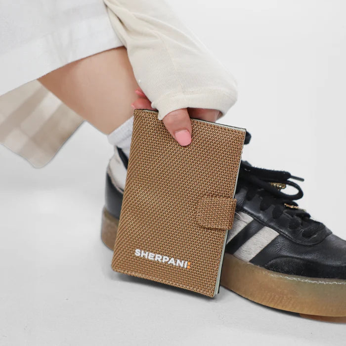 Woman holding a Sherpani Vienna Sand Anti-theft Passport Wallet against white background. #color_sand-tan