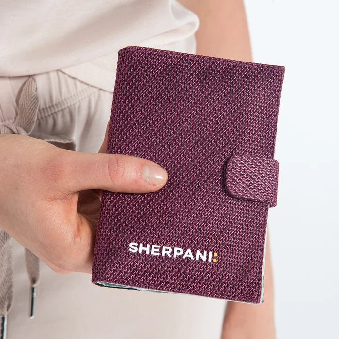 Woman holding a Sherpani Smoky Orchid Carbon Black Anti-theft Passport Wallet against white background. #color_smoky-orchid-pink