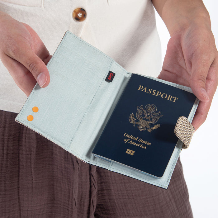 A woman holding a Sherpani Vienna Straw Beige Anti-theft Passport Wallet against a white background.  #color_straw-beige
