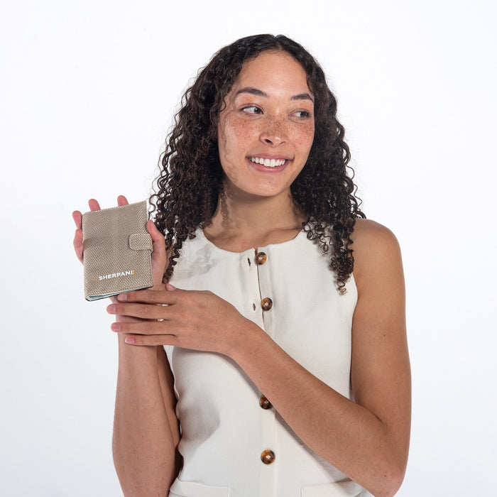 A woman holding a Sherpani Vienna Straw Beige Anti-theft Passport Wallet against a white background.  #color_straw-beige