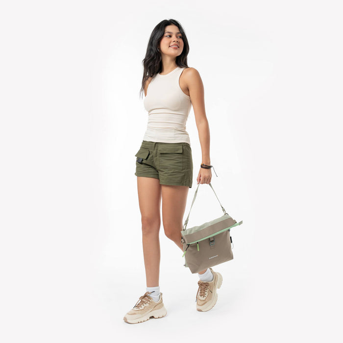 Woman holding a Sherpani Viso Desert Aloe Foldover Bag by adjustable strap against a white backdrop. #color_desert-aloe