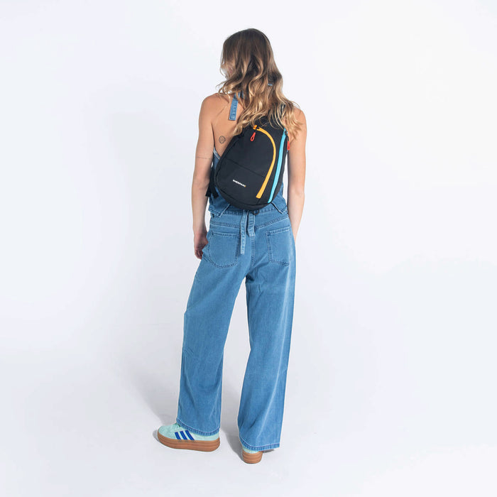 A woman wearing a Sherpani Wayfarer Chromatic Black Convertible Sling on her back against white background.  #color_chromatic-black