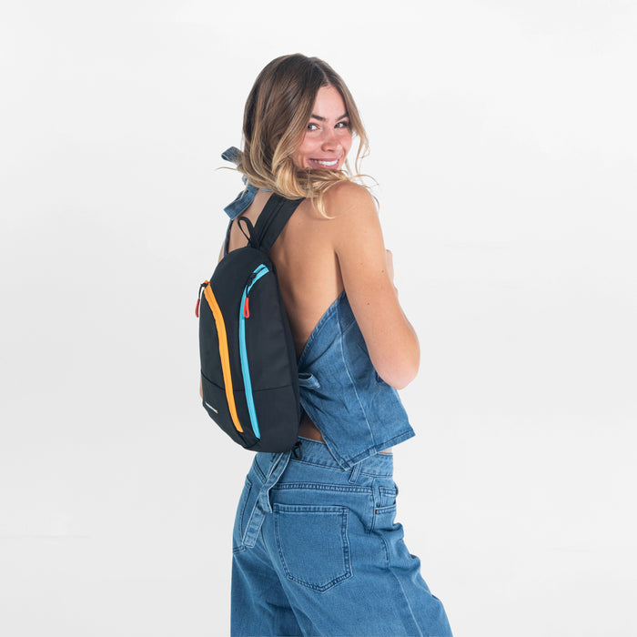 A woman wearing a Sherpani Wayfarer Chromatic Black Convertible Sling on her front against white background.  #color_chromatic-black