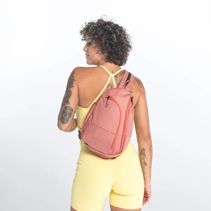 A woman wearing a Sherpani Wayfarer Desert Pink Convertible Sling on her back against white background.  #color_desert-pink