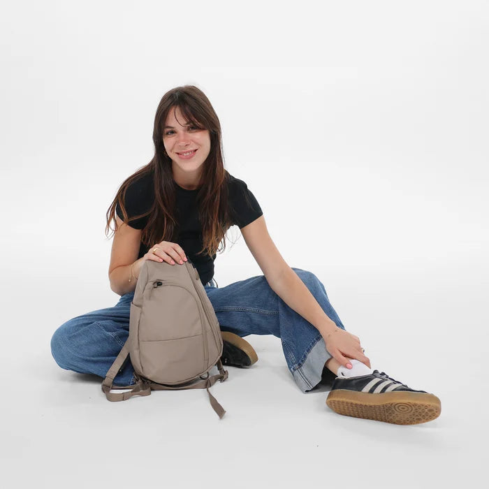 A woman holding a Sherpani Wayfarer Dune Convertible Sling on her Front on the ground. #color_dune-tan
