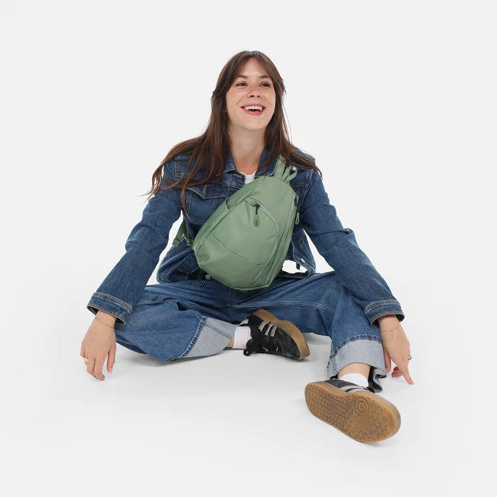 A woman wearing a Sherpani Wayfarer Olivine Convertible Sling on her front against white background. #color_olivine-green