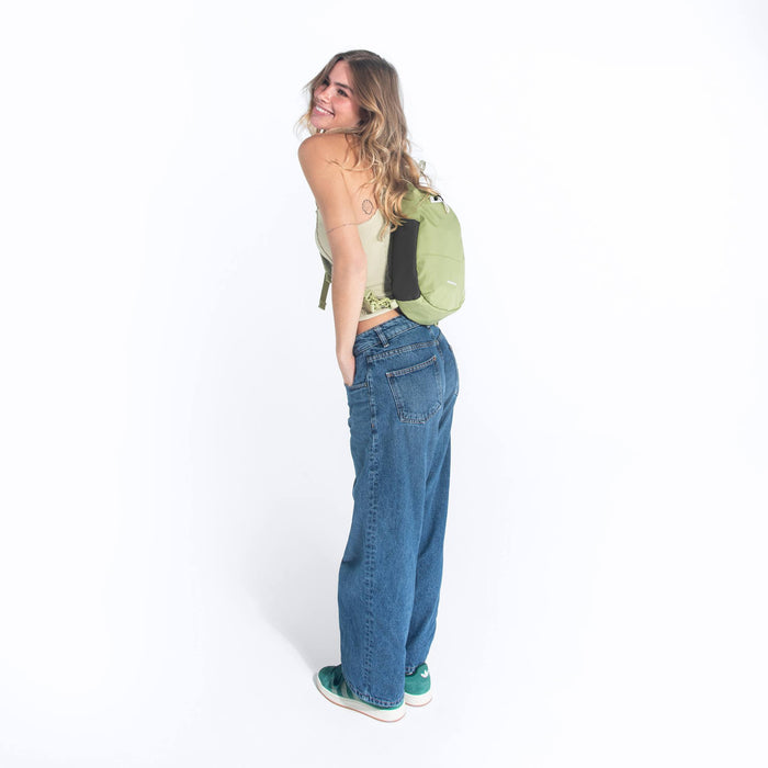 A woman wearing a Sherpani Wayfarer Palm Green Convertible Sling on her back against white background.  #color_palm-green