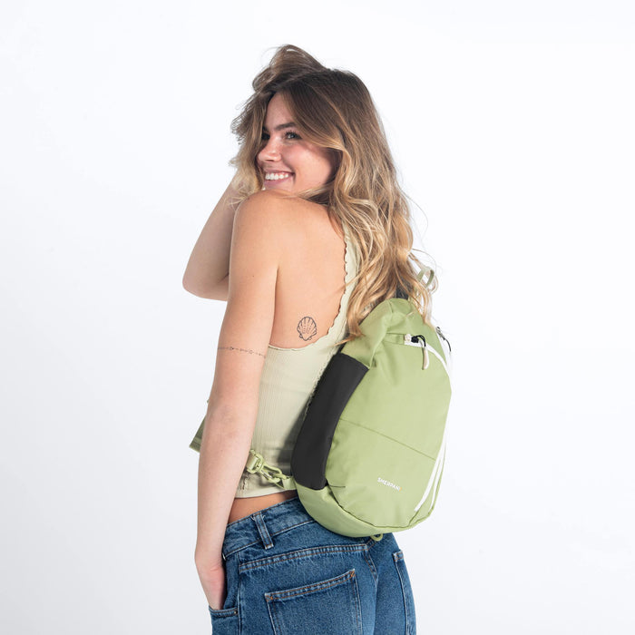 A woman wearing a Sherpani Wayfarer Palm Green Convertible Sling on her back against white background.  #color_palm-green