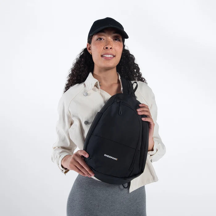 A woman wearing a Sherpani Wayfarer Raven Black Convertible Sling on her front against white background.  #color_raven-black