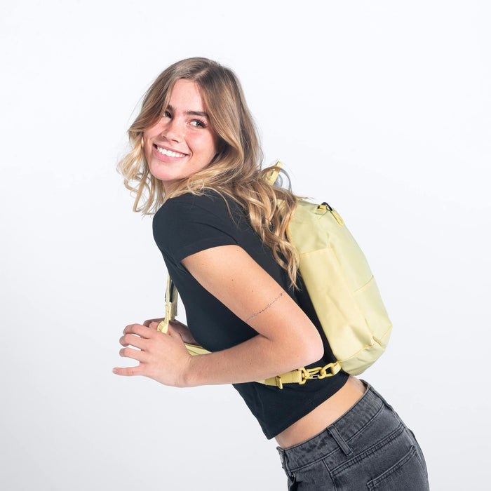 A woman wearing a Sherpani Wayfarer Sol Yellow Convertible Sling on her back against white background.  #color_sol-yellow
