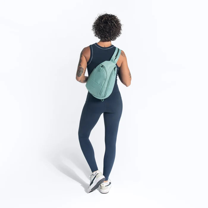 A woman wearing a Sherpani Wayfarer Surf Blue Convertible Sling on her back against white background.  #color_surf-blue
