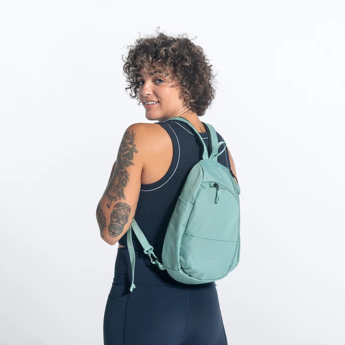 A woman wearing a Sherpani Wayfarer Surf Blue Convertible Sling on her front against white background.  #color_surf-blue