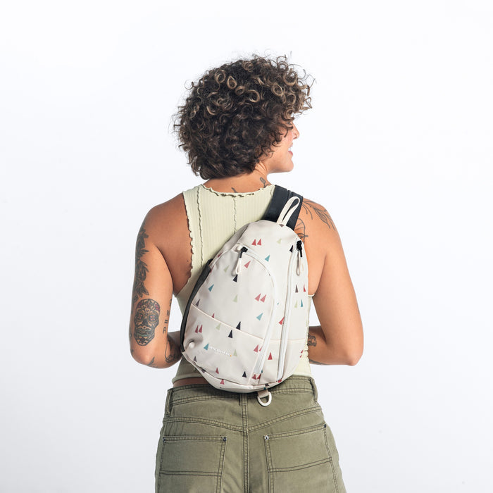 A woman wearing a Sherpani Wayfarer Terrazzo Print Convertible Sling on her back against white background.  #color_terrazzo-print