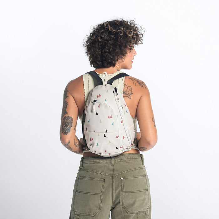 A woman wearing a Sherpani Wayfarer Terrazzo Print Convertible Sling on her back against white background.  #color_terrazzo-print