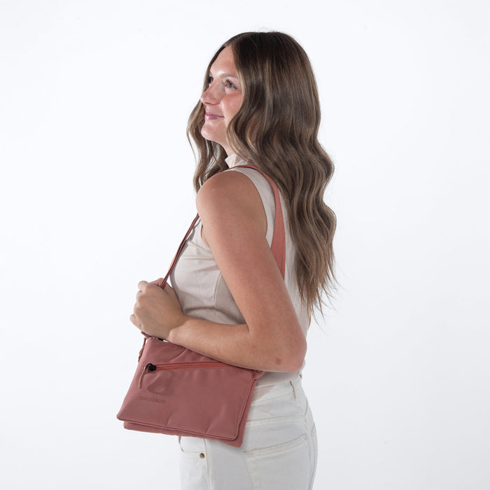 Woman wearing a Sherpani Zoom Desert Pink Slim RFID Crossbody against white background. #color_desert-pink