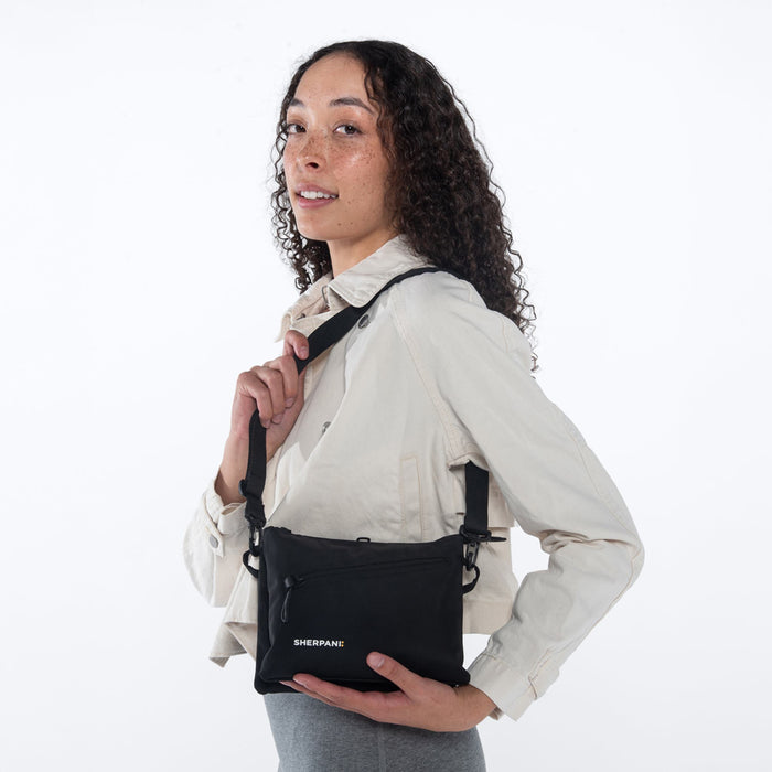 Woman wearing a Sherpani Zoom Raven Black Slim RFID Crossbody against white background. #color_raven-black